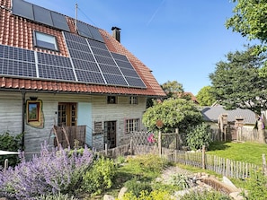 Ein Haus mit Solaranlage auf dem Dach, einem Holzzaun und einem Garten mit verschiedenen Pflanzen.