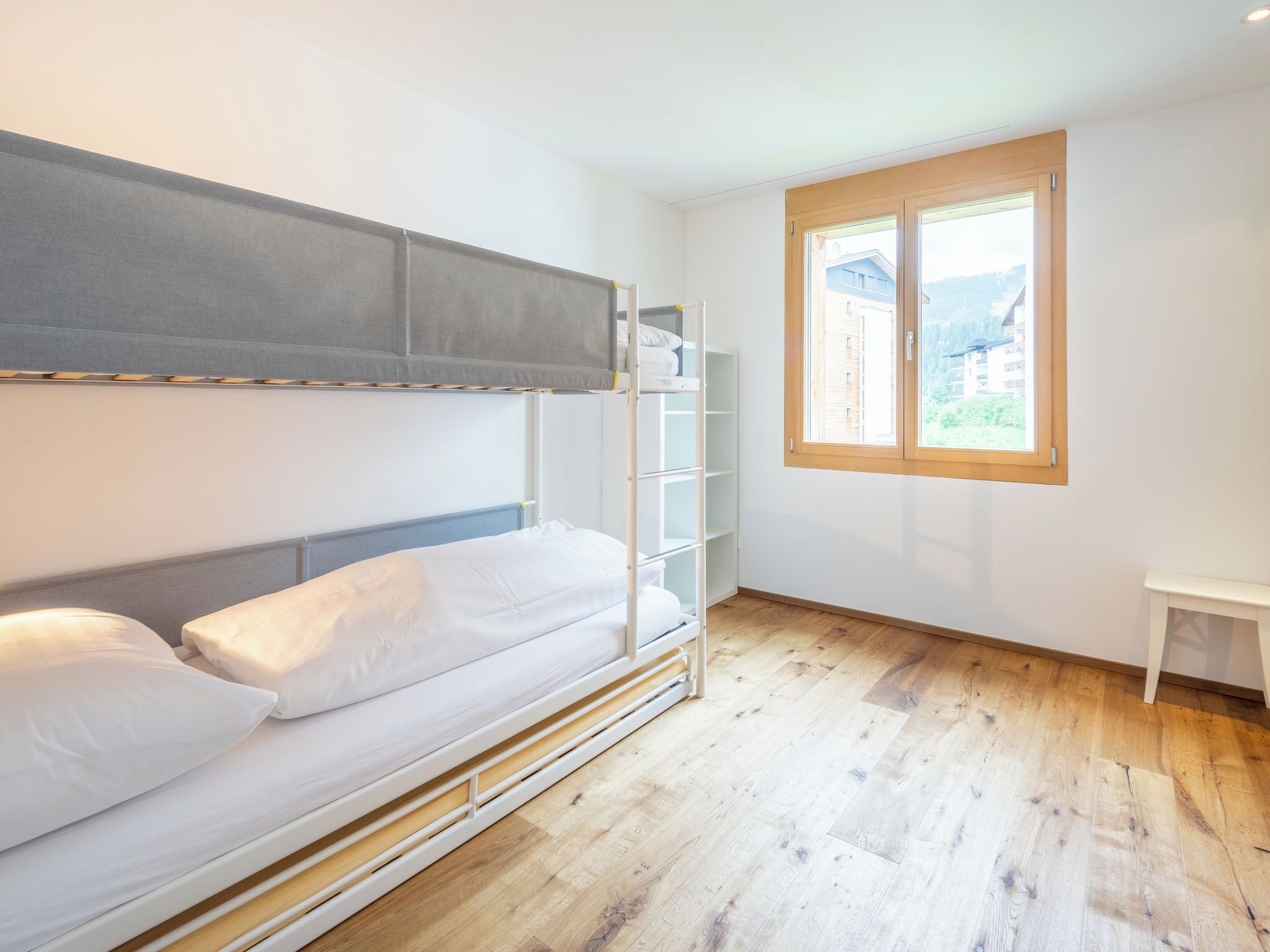 A bunk bed with a headboard, a window with a view, and a small white table.