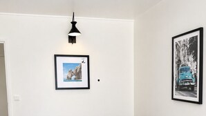 A single-bed room with a white mattress, a black headboard, a wall-mounted light, and two framed pictures. - Charming Studio with Terrace and Garden in the 17th arrondissement, 09 (Paris)