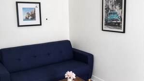 A room with a dark blue sofa, a small wooden side table with a vase, a black floor lamp, and two framed pictures on the wall. - Charming Studio with Terrace and Garden in the 17th arrondissement, 09 (Paris)