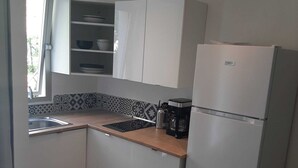 A compact kitchen with white cabinets, a built-in sink, a coffee maker, and a refrigerator. - Charming Studio with Terrace and Garden in the 17th arrondissement, 09 (Paris)