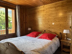 A wooden cabin bedroom with a bed, two bedside lamps, and a window with a view of greenery. - 300m from ski slopes, 1st floor, tv, ski locker, 57m², Pralognan-la-Vanoise (Pralognan-la-Vanoise)
