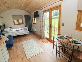 A cozy room with a bed, a table with plates and glasses, a blue sofa, and a view of a green garden through a door.