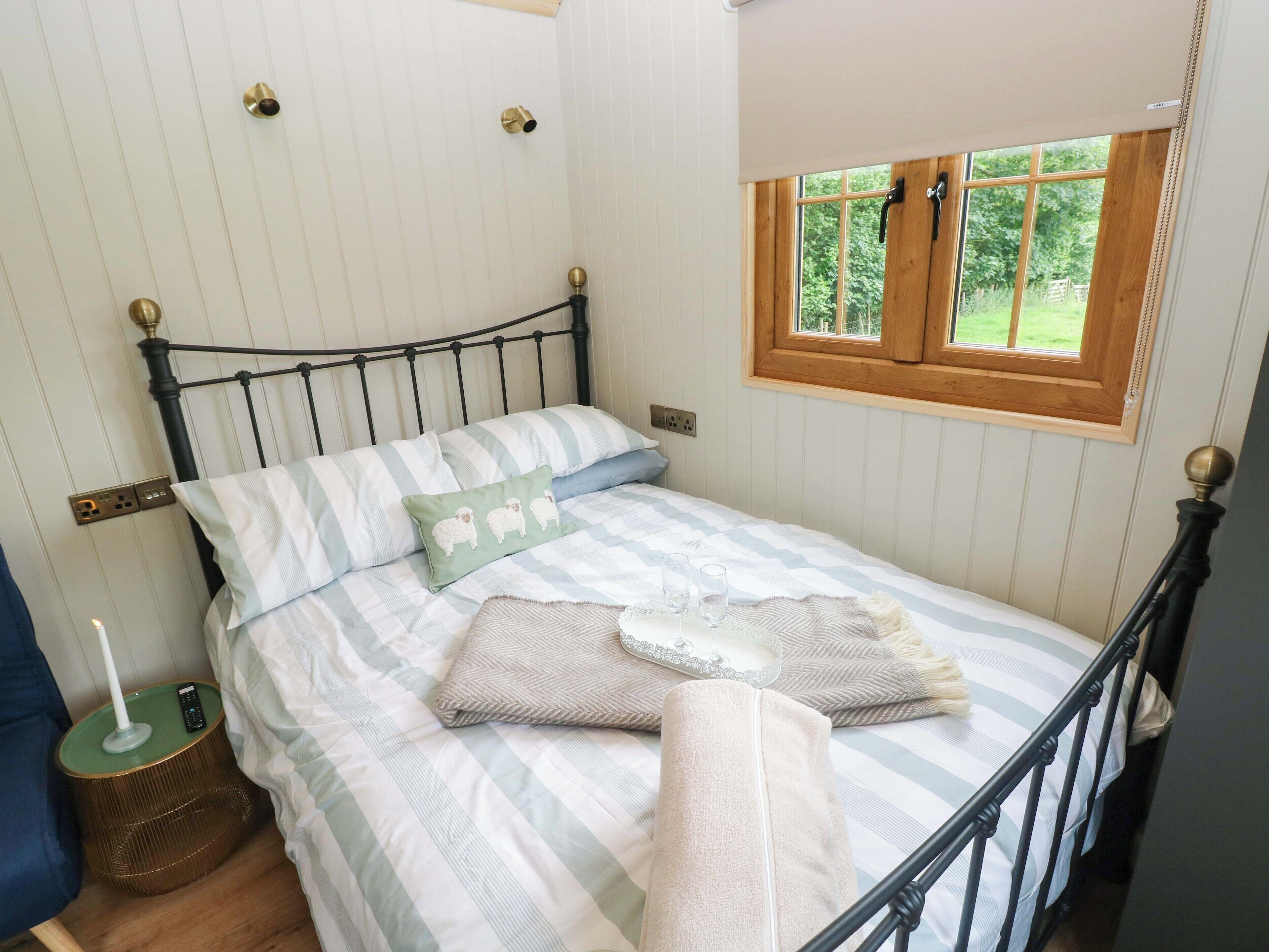 A neatly made bed with striped bedding, a bedside table with a lamp, and a window with a wooden frame.