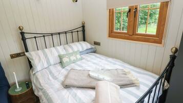 A neatly made bed with striped bedding, a bedside table with a lamp, and a window with a wooden frame.