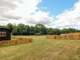 A fenced outdoor area with a small building, a wooden fence, and a grassy field.