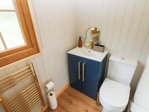 A bathroom with a white toilet, a blue cabinet with gold handles, a mirror, and a wooden towel rack. - Cwtch Y Bugail 2 (Llandeilo)