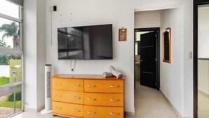 A hotel room with a large flat-screen TV mounted on the wall, a wooden dresser with drawers, and a door leading to another room. - Family-Friendly Country Retreat with a Pool and Garden (Huaxtla)