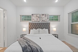 A bedroom with a large bed, two bedside tables with lamps, a tufted headboard, and two abstract paintings above the bed. - Luxury Modern Retreat in Houston - near NRG Stadium & Hobby Airport (Houston)