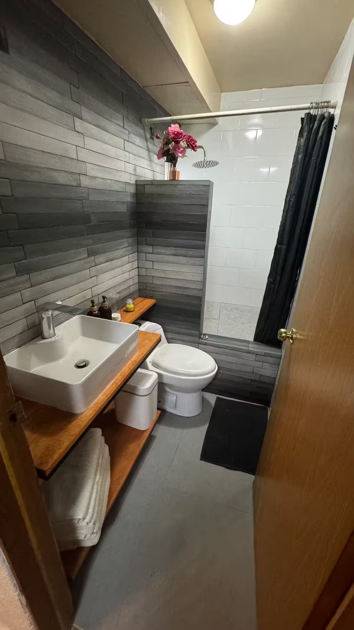 Une salle de bain moderne avec un mur recouvert de carreaux gris et blancs, un lavabo blanc, des toilettes et une douche avec un rideau noir.