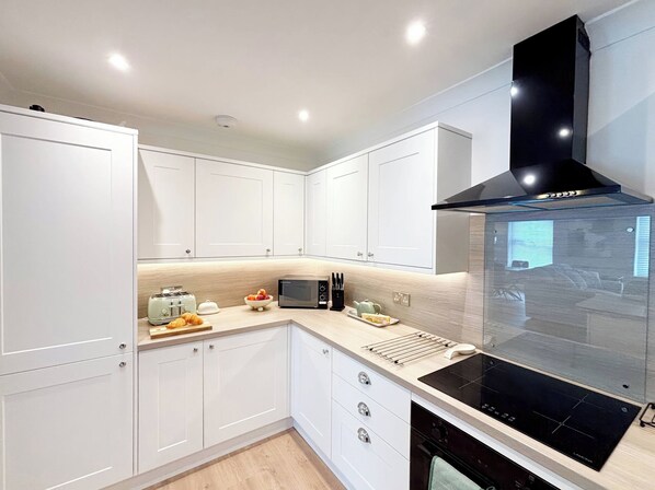 A modern kitchen with white cabinets, a black range hood, and a built-in oven.