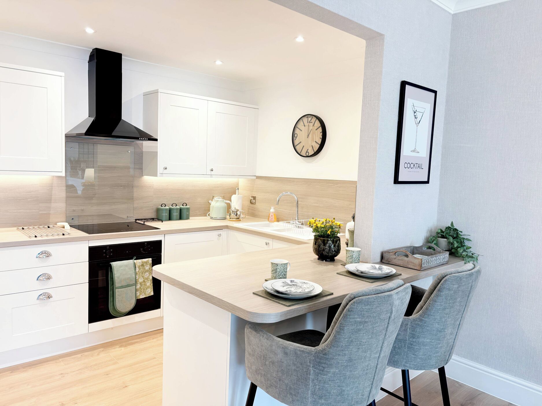 Une cuisine moderne avec des meubles blancs, un îlot central, une horloge et une œuvre d’art encadrée au mur.