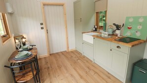 A compact kitchen with wooden flooring, a dining area with a table and chairs, and a green refrigerator. - Cwtch Y Bugail 1 (Llandeilo)