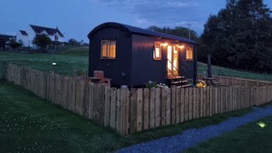 A small, dark-colored mobile home with a porch, a wooden fence, and a grassy yard. - Cwtch Y Bugail 1 (Llandeilo)