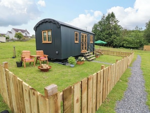 Eine kleine, dunkel gefärbte Holzhütte mit Veranda, Holzstühlen und einem Kiesweg.