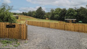 A gravel driveway leading to a wooden gate with a sign, surrounded by a fence and trees. - Cwtch Y Bugail 1 (Llandeilo)