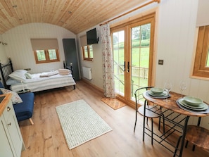 Ein Zimmer mit einem Bett, einem Tisch mit Tellern und Gläsern, einem blauen Sofa und Blick auf eine grüne Landschaft durch eine Tür.