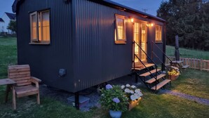 A small, dark-colored cabin with a porch, wooden steps, and a bench. - Cwtch Y Bugail 1 (Llandeilo)
