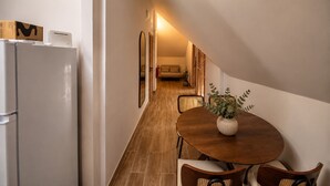 Um corredor estreito com piso de madeira, uma mesa de jantar com cadeiras, um refrigerador e um espelho.