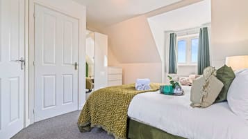 A hotel room with a bed, a window with curtains, a desk with a lamp, and a mirror.