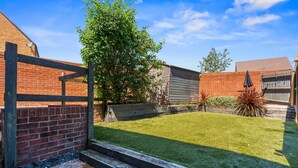 Un jardin avec une pelouse bien entretenue, une clôture en bois et un mur en briques.