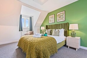 Quarto de hotel com cama, duas mesas de cabeceira, uma janela e paredes verdes.