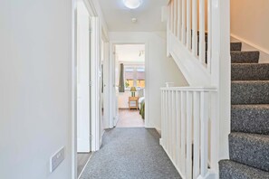 A hallway with a carpeted floor, white walls, and a staircase with grey carpeted steps.