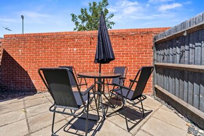 A patio with a brick wall, a wooden fence, and a table with four chairs. - 4 BR House with Private Garden, 2X FREE Parking (Basingstoke)