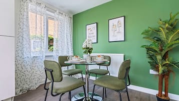 A dining area with a round table, four chairs, a potted plant, and two framed pictures on the wall.
