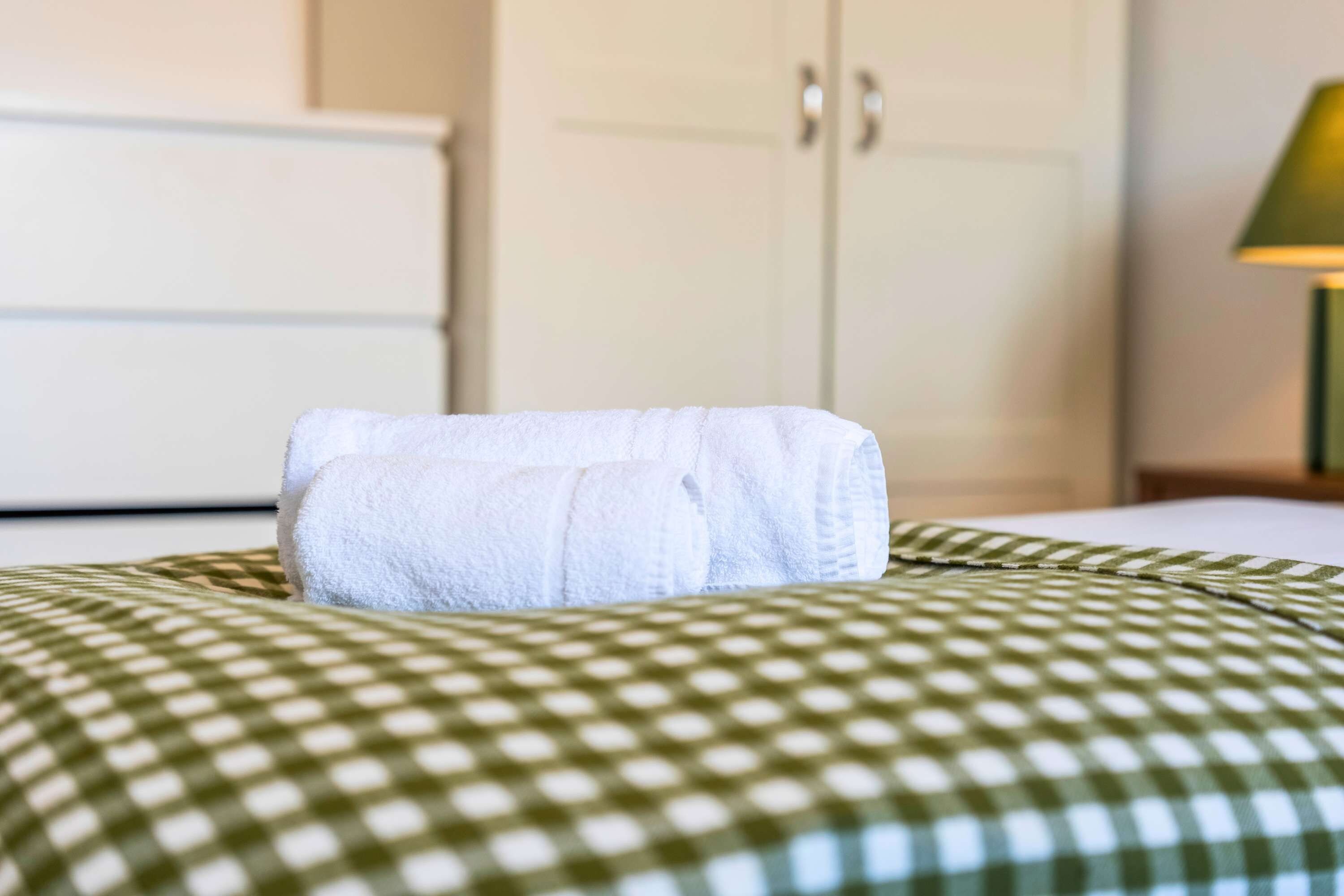 Un lit recouvert d’une couverture à carreaux verts et blancs, avec une serviette blanche posée dessus.