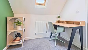 Une pièce de taille modeste avec un plafond en pente, un radiateur, un bureau avec une chaise et des étagères ornées de plantes.