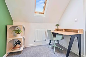 Ein gemütlicher Raum mit schrägverdeckter Decke, Heizkörper, Schreibtisch mit Stuhl und Regale mit Pflanzen.