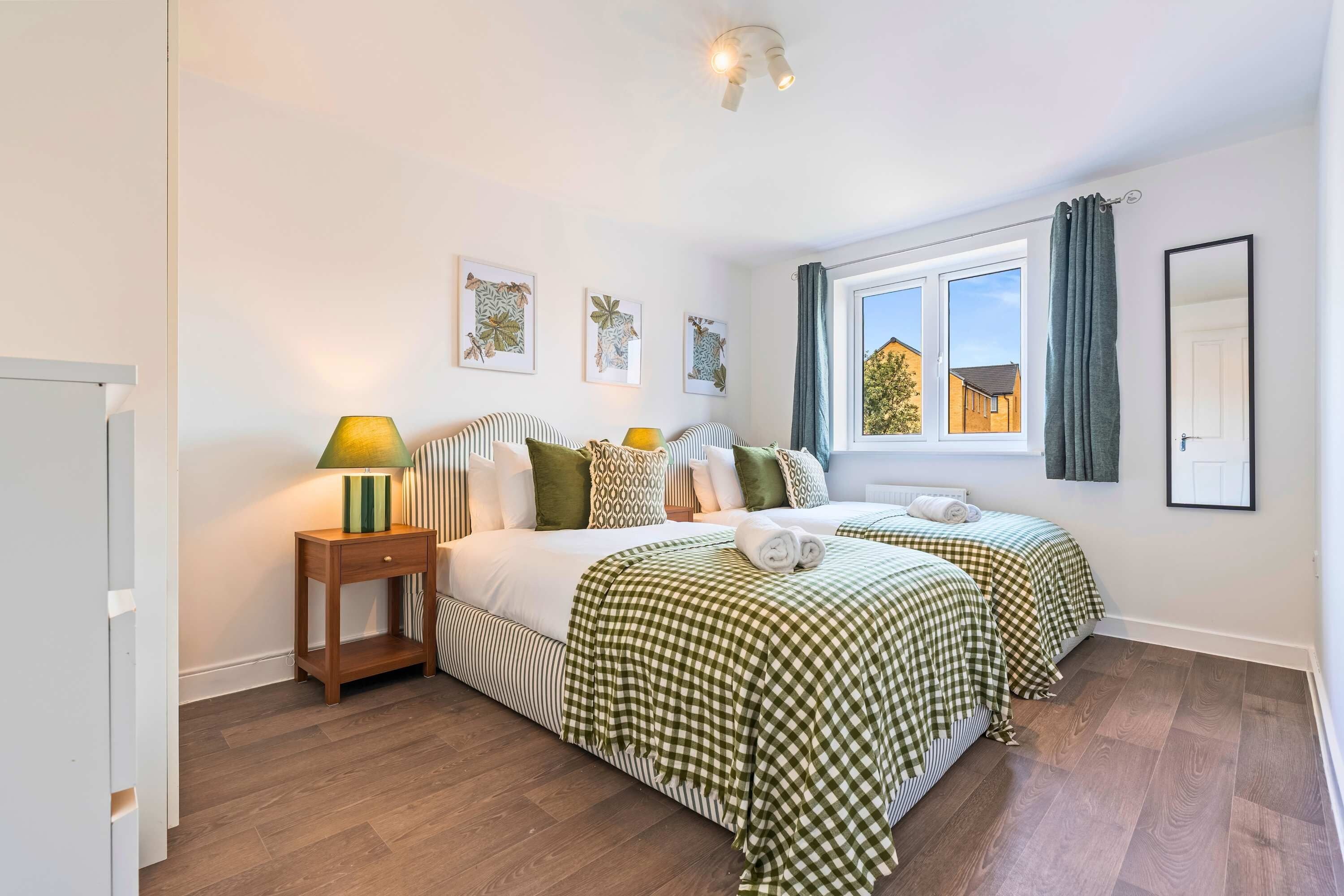 A bedroom with two beds, a nightstand, a window with curtains, and a mirror.