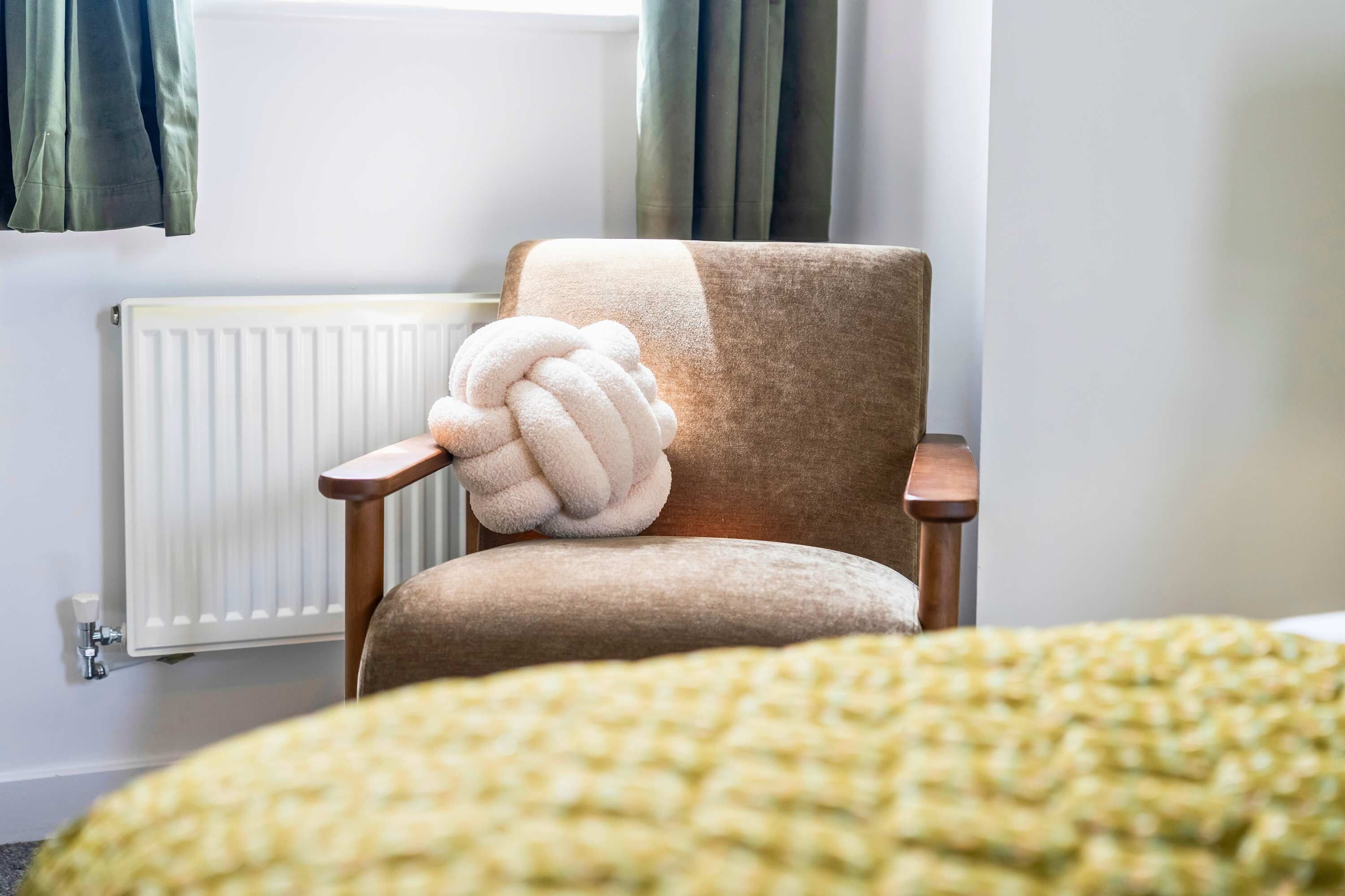 A room with a chair, a radiator, and a bed with a blanket.