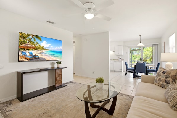A living room with a TV, a glass coffee table, a sofa, and a dining area with chairs. - Spacious duplex, dog friendly & full kitchen (Englewood)