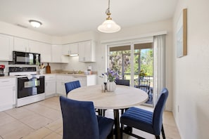 A modern kitchen with white cabinets, a black microwave, and a stove. There is a dining area with a round table and blue chairs. - Spacious duplex, dog friendly & full kitchen (Englewood)