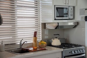 A kitchen with a microwave, stove, sink, and a window with blinds. - Bright Studio w/ Workspace & Marina View in Cas en Bas, Gros Islet (Gros Islet)