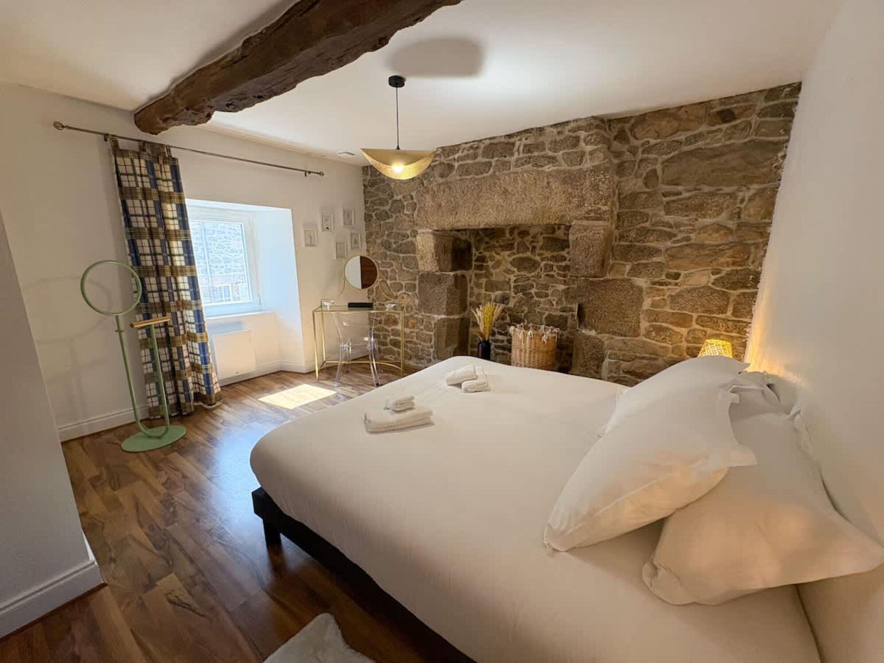 Ein Schlafzimmer mit Steinwand, einem Bett mit weißen Bettwäsche, einer Pendelleuchte und einem Fenster mit Vorhängen.