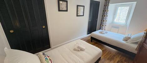 A bedroom with two beds, a window, and a door with shutters.