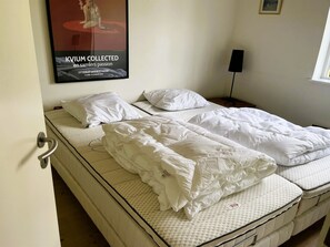 Ein Zimmer mit zwei Betten, einem Poster an der Wand, einer Tür und einem Fenster.