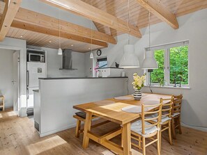 Una cuina moderna amb bigues de fusta, una zona de menjador amb taula i cadires de fusta, i una finestra amb vista a vegetació.