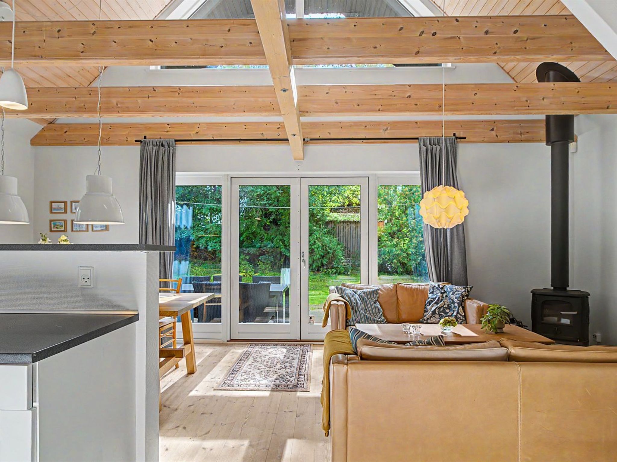 A modern kitchen with a dining area, a sofa, and a large window with curtains.