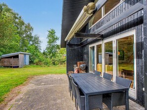 A wooden house with a patio, outdoor seating, and a barbecue grill.