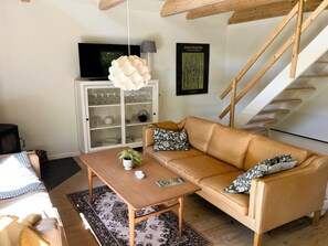 Ein Wohnzimmer mit Sofa, Couchtisch, einer Schrank mit Glastüren, einer Treppe und einer Pendelleuchte.