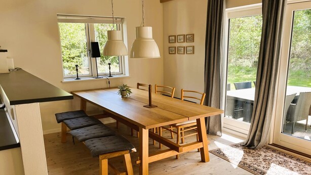Un comedor con una mesa de madera, bancos, lámparas colgantes y vistas amplias a través de grandes ventanales.