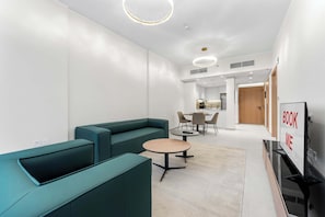 A modern hotel lobby with teal seating, a round table, and a 'BOOK ME' sign. - Free housekeeping visits during your stay - StayShort - Stunning 1BR Retreat in JVC that Sleeps 2! (JVC)