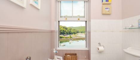 A bathroom with a window view of a lake, a toilet, a towel rack, and a small shelf with a basket.