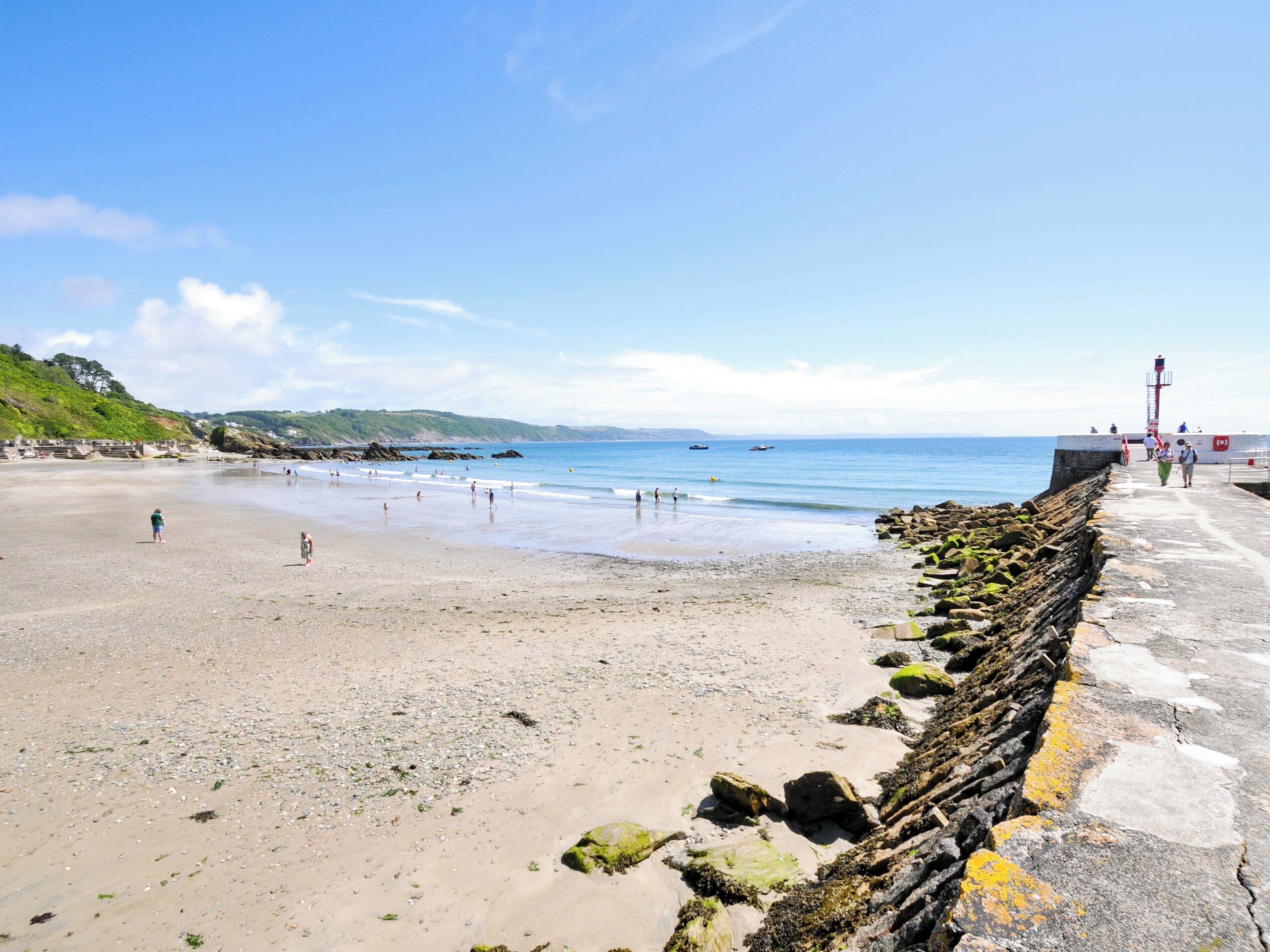A beach with a rocky breakwater, a lighthouse, and a clear sky.