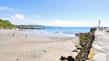 A beach with a rocky breakwater, a lighthouse, and a clear sky.