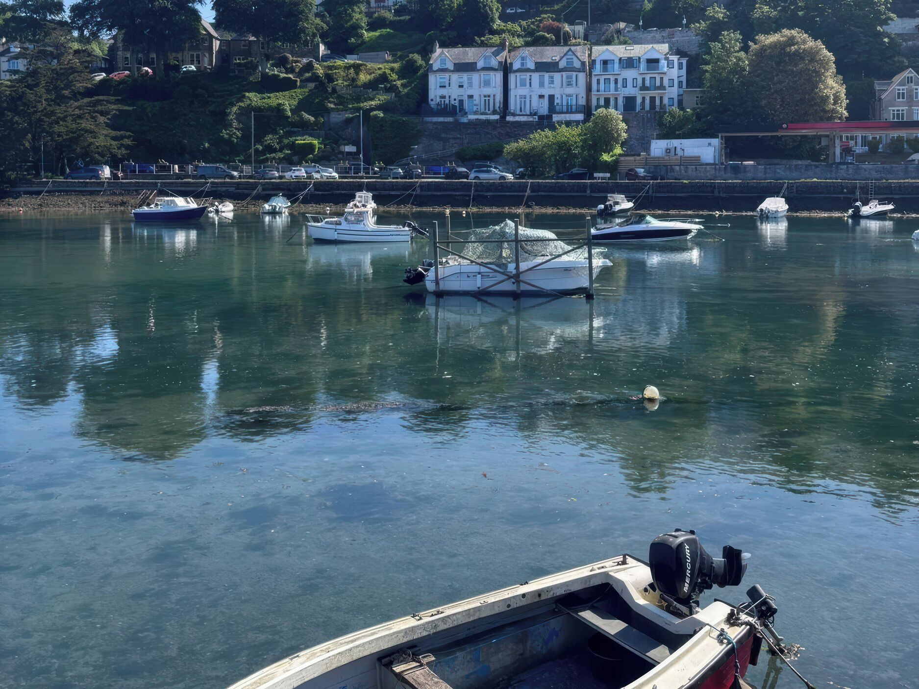 A marina with several boats docked, a building with multiple windows in the background, and a clear view of the water.